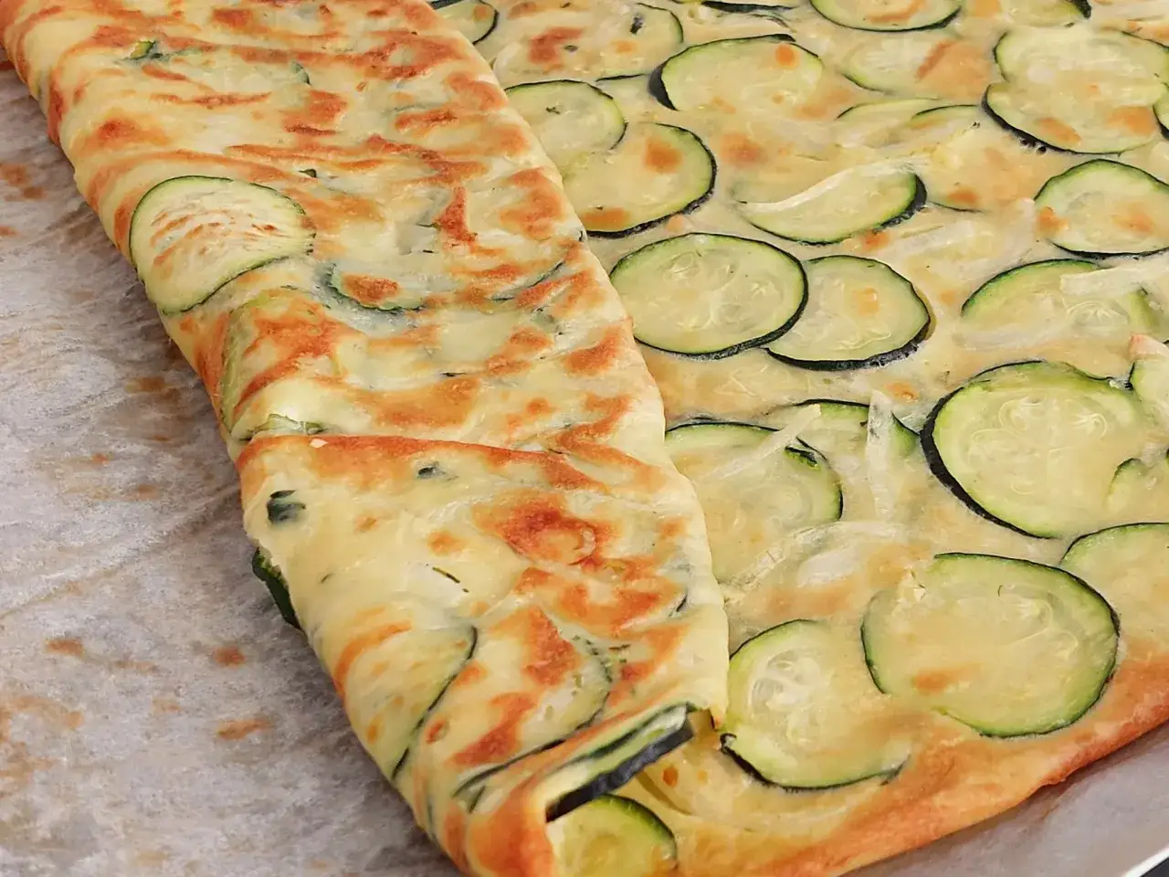 Złocista tortilla z cukinii, z widocznymi plasterkami warzywa i delikatnie zarumienionym ciastem, wygląda apetycznie.
