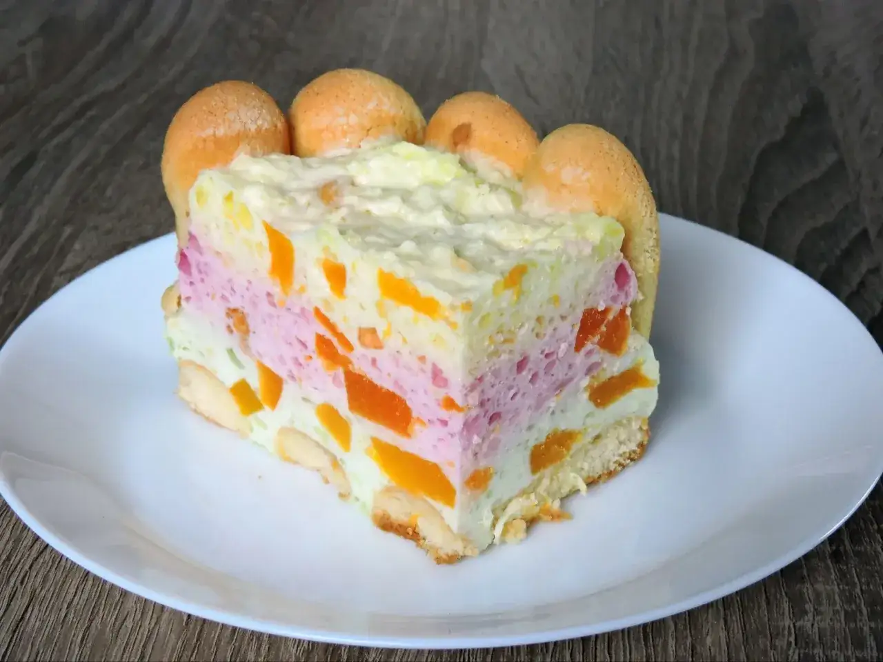 Kolorowe ciasto bez pieczenia z biszkoptami i owocami, podane na białym talerzu.