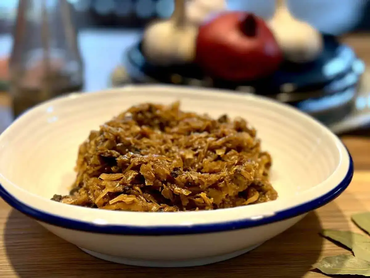 Pyszny bigos wigilijny przepis. Aromatyczna kapusta z grzybami i śliwkami w białej misce, gotowa na świąteczny stół.
