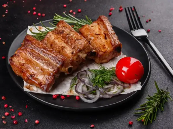 Soczyste żeberka z piekarnika, idealne na obiad. Podane z pomidorkiem, cebulą i rozmarynem.