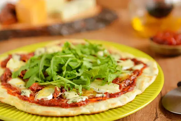 Pyszna pizza z patelni z rukolą i serem pleśniowym, podana na zielonym talerzu.