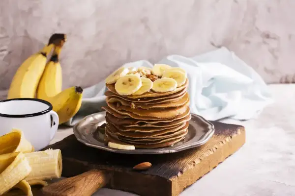 Stos naleśników z plasterkami banana i orzechami. Idealny pomysł, co zrobić z bananów na pyszne śniadanie.