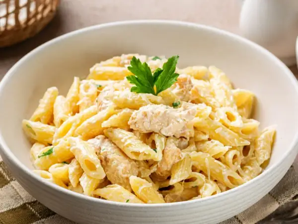 Penne z kremowym sosem i kawałkami kurczaka, posypane parmezanem i udekorowane natką pietruszki. Pyszny makaron z kurczakiem.