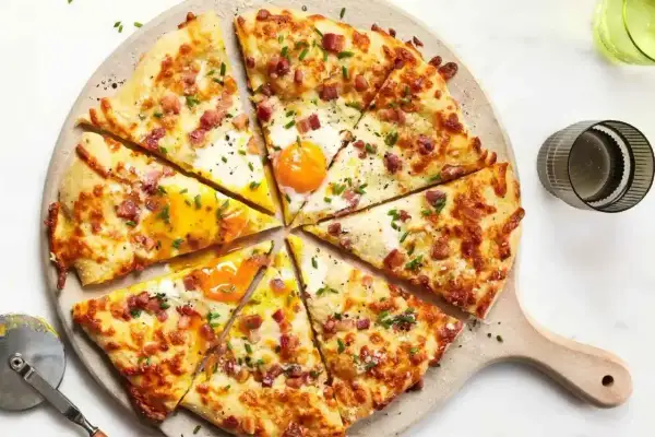 Pyszna pizza z jajkiem i boczkiem, posypana szczypiorkiem. Idealne dodatki do pizzy, które zachwycą każdego smakosza.