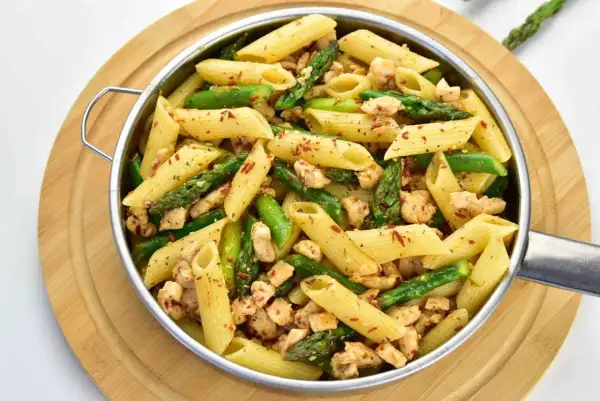 Penne z kurczakiem i szparagami, posypane papryką. Pyszne danie na obiad.