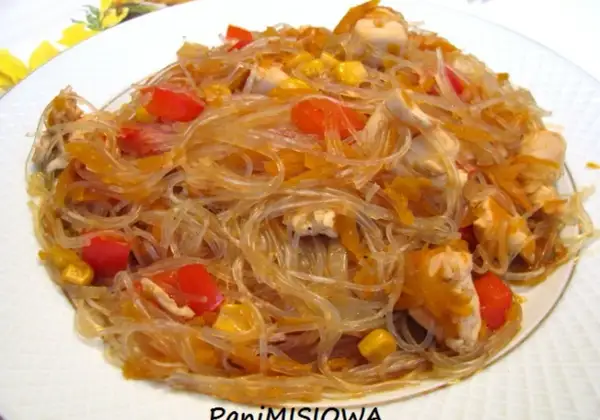 Pyszny makaron sojowy z kurczakiem, papryką i kukurydzą na białym talerzu.