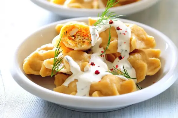 Pyszne, szybkie dania bezmięsne na obiad: pierogi z farszem warzywnym, polane sosem jogurtowym z koperkiem i posypane pieprzem.