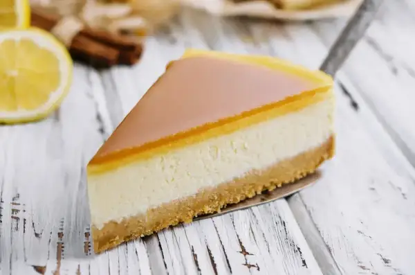 Pyszny sernik z mascarpone na kruchym spodzie, z delikatną galaretką na wierzchu. Obok cytryna i laski cynamonu.