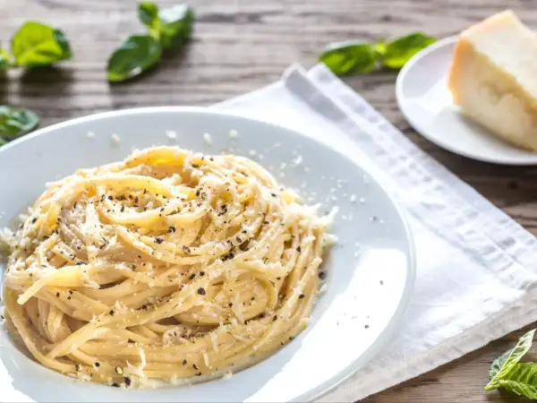 Szybki obiad z makaronem: spaghetti posypane parmezanem i pieprzem, obok kawałek sera i listki bazylii.