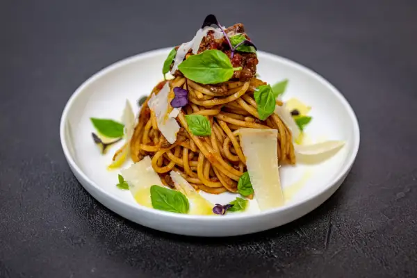 Pyszne spaghetti alla norma z sosem pomidorowym, bakłażanem, bazylią i płatkami parmezanu.