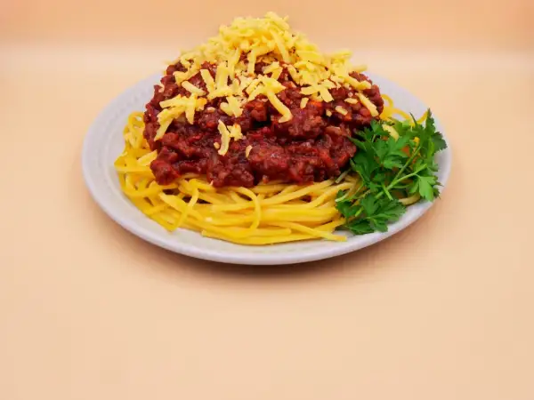 Pyszne spaghetti z mięsem mielonym, posypane żółtym serem i udekorowane gałązką natki pietruszki.