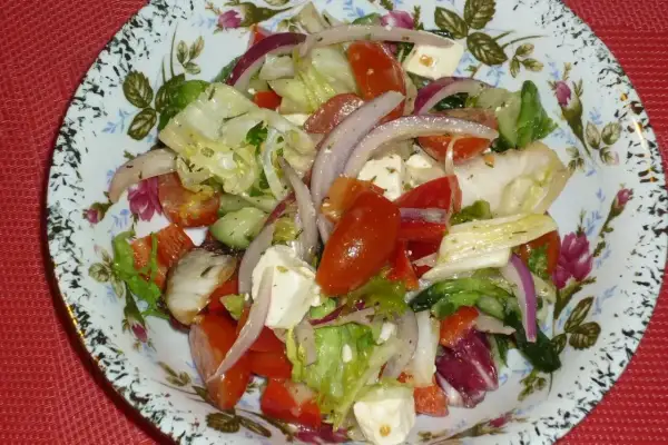 Pyszna sałatka z mix sałat, pomidorów, ogórka, czerwonej cebuli i sera feta, podana na ozdobnym talerzu.